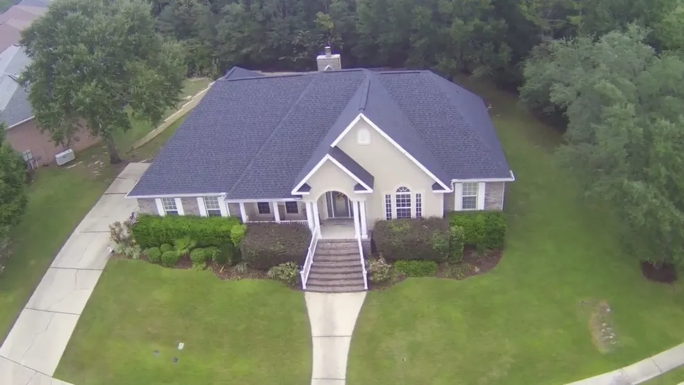 Aerial front view of tan brick home with dark charcoal hip shingle roof and covered porch in Navarre FL by H&R Roofing and Construction