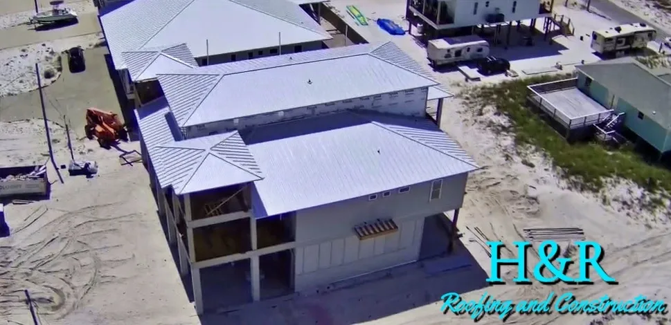 Aerial top-down view of white metal roof installation in progress on beachfront stilt home on Navarre Beach FL by H&R Roofing and Construction